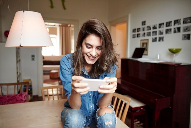 Young woman sitting on dining table reading smartphone texts