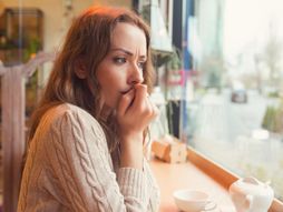 Nervous worried young woman biting nails and looking away sitting alone in a coffee shop zbunjena uplašena devojka žena kafić