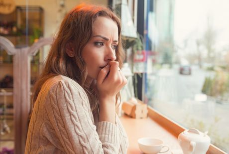 Nervous worried young woman biting nails and looking away sitting alone in a coffee shop zbunjena uplašena devojka žena kafić