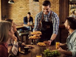 konobar, Happy waiter serving food to group of cheerful friends in a pub.
