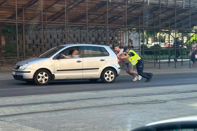 Policajac i mladić pomažu starijem čoveku sa pokvarenim autom