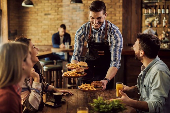 konobar, Happy waiter serving food to group of cheerful friends in a pub.