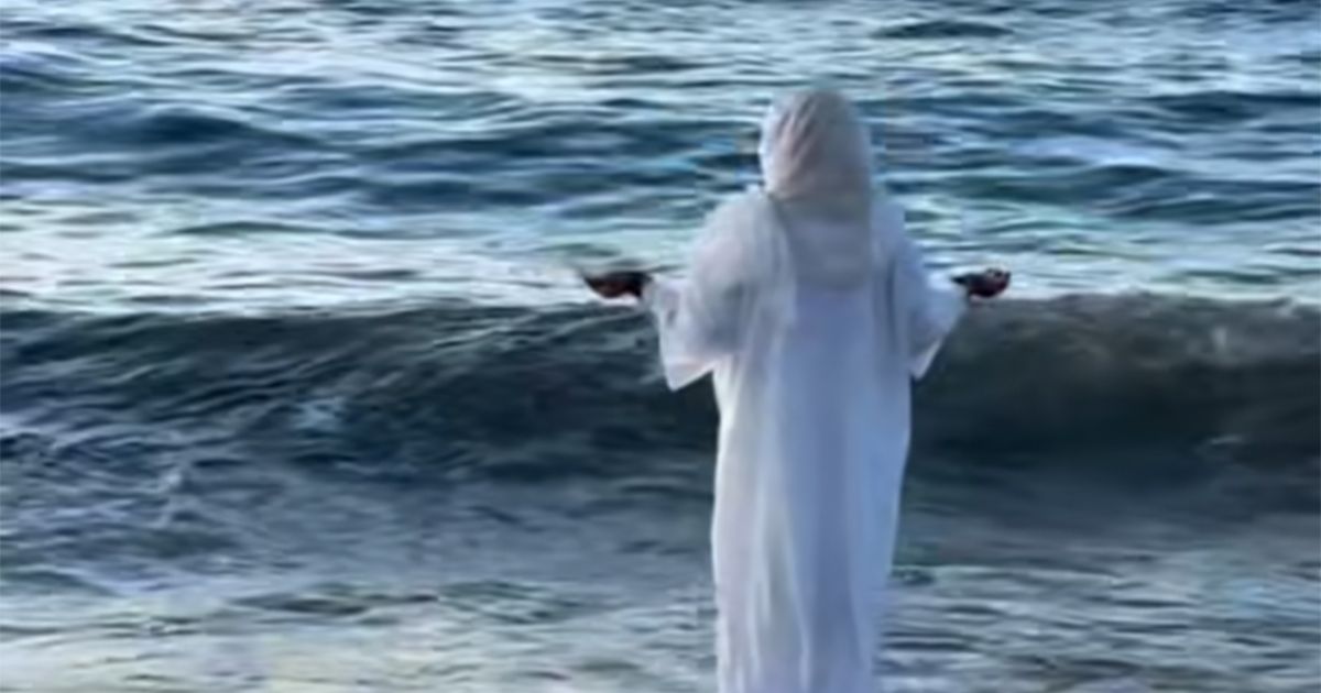 Misteriozna žena u belom stoji nepomično na plaži sa ispruženim rukama ...