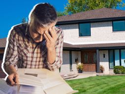 čovek koji se drži za glavu, papiri i neka kuća